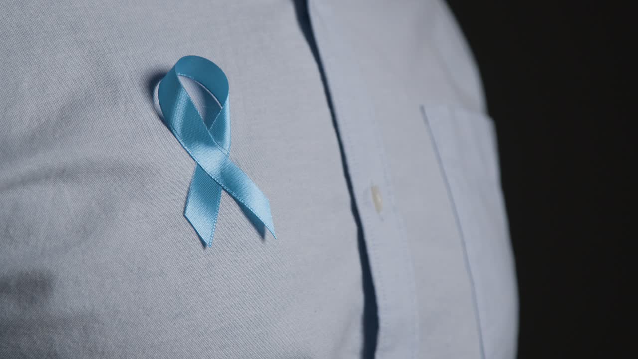 Close Up Of Man Putting On Blue Ribbon Badge Symbolizing Awareness Of Men's Health And Cancer Onto Shirt