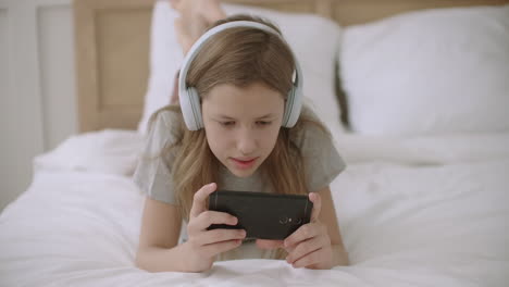 teen girl is surfing internet on smartphone reading information from site lying on bed in home after school