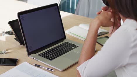 mujer de negocios caucásica con máscara facial usando una computadora portátil con pantalla en blanco en la oficina