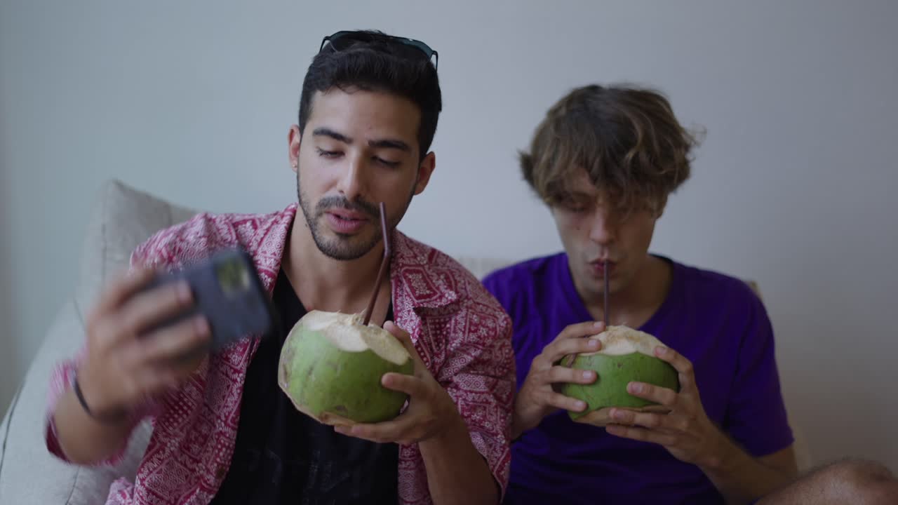 Two young men taking a selfie and enjoying coconut drinks
