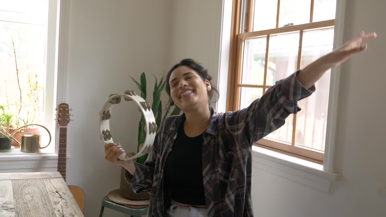 feliz cantante caribeña con el brazo levantado sacudiendo y tocando la pandereta y bailando