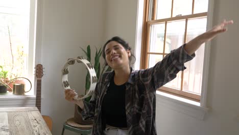 happy caribbean girl musician with arm raised shaking and playing tambourine and dancing