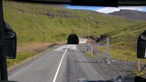 driving in countryside of iceland, road and tunnel under green hills on sunny day, bus driver pov