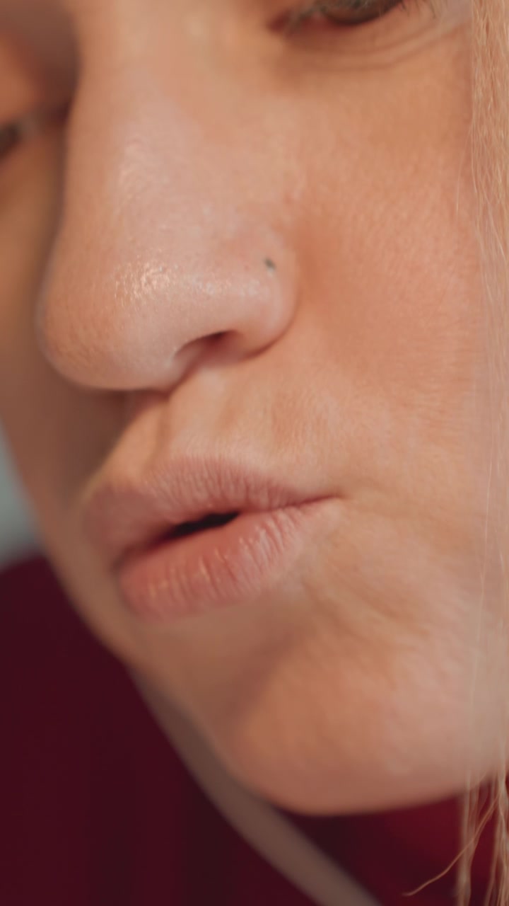Close up of woman mouth and nose as woman speaks with subtle lip movements. Small mole is present near her nostril. Background features red fabric or clothing suggesting