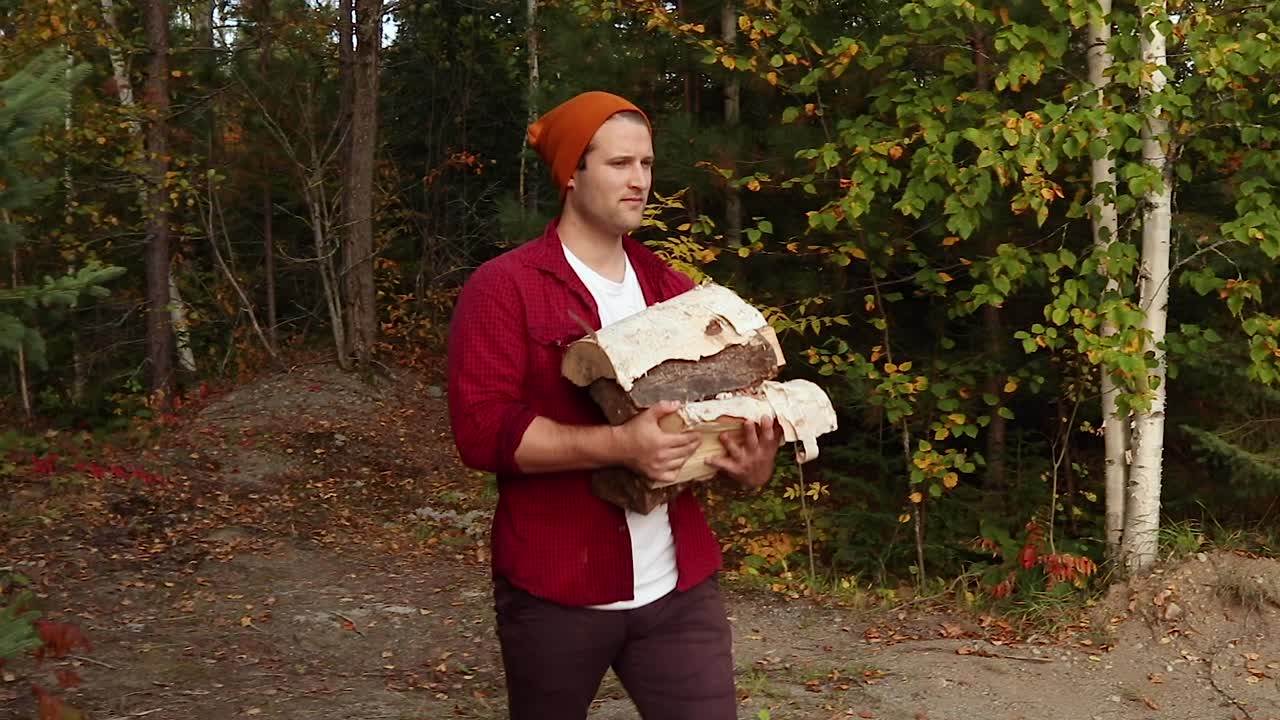 Handsome young man carrying a large amount of logs to a fire pit during the peak fall season in Canada