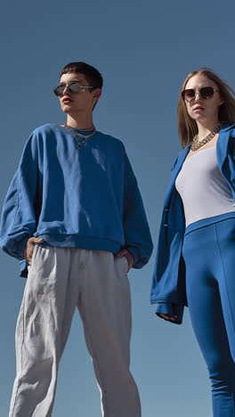 stylish young man with sunglasses and chains posing under a clear blue sky