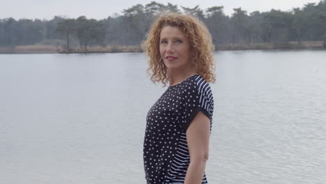 Older-woman-standing-near-lakeside-and-turning-towards-camera