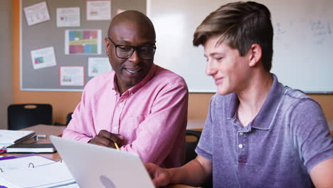 high school tutor giving male student using laptop one to one tuition at desk