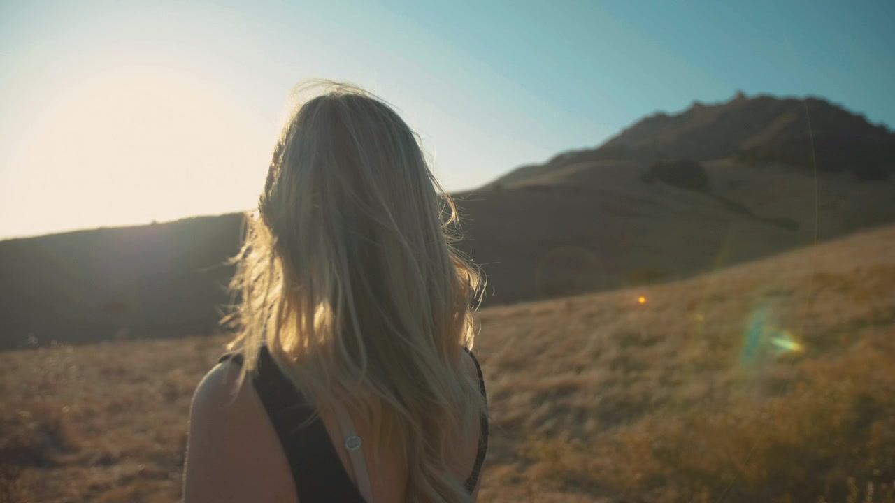 Giovane Donna con Capelli Biondi in Piedi su una Collina al Tramonto