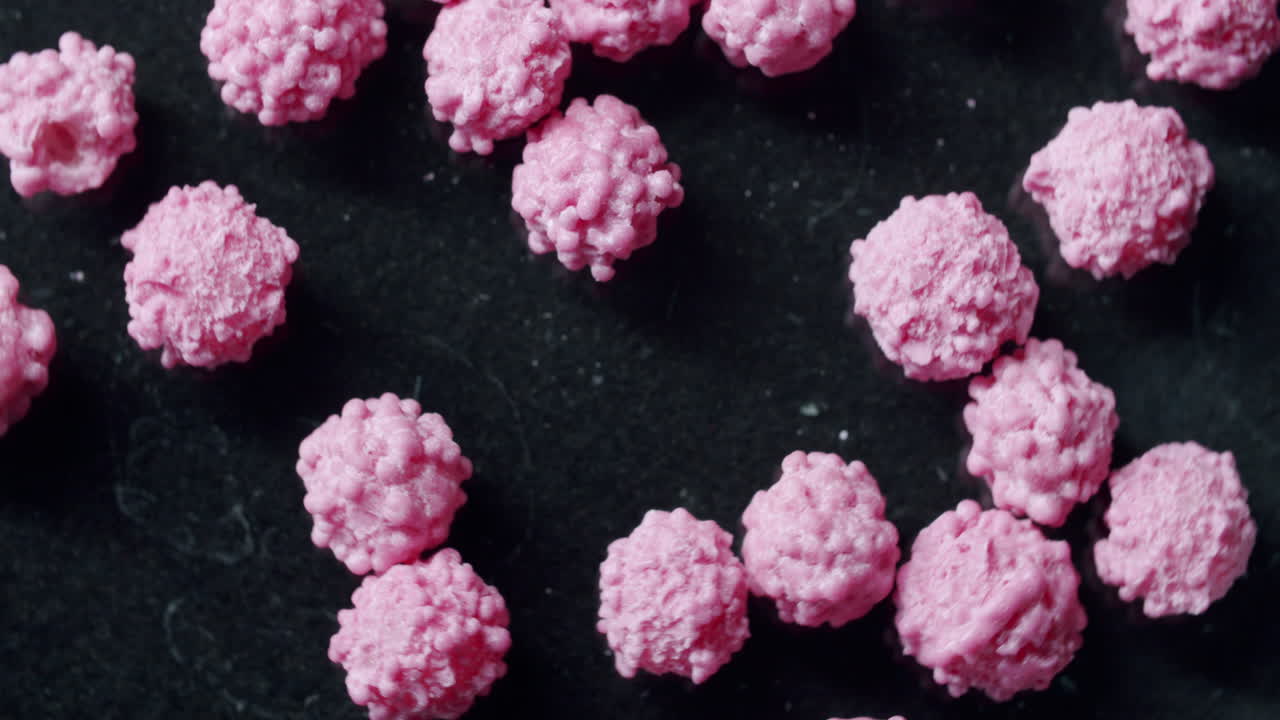 Close up shot of pink cells on a black surface with light from the left. Black surface spinning. Particles not moving