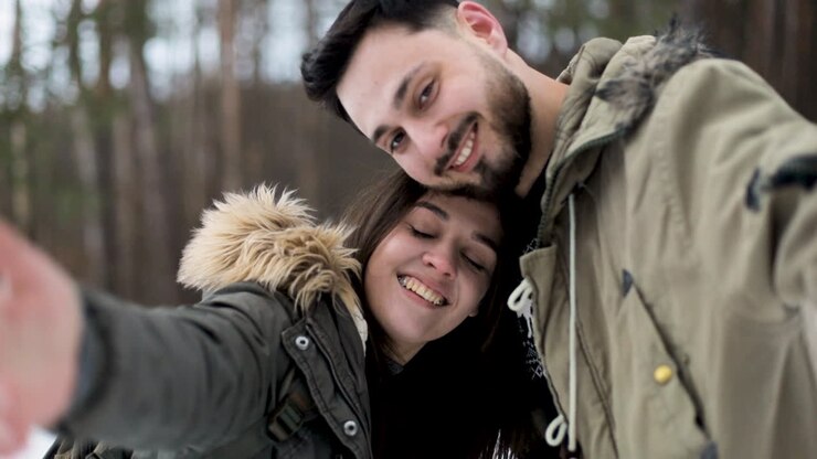 Couple caucasien prenant des selfies et se câlinant dans une forêt enneigée