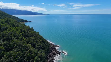 aerial drone footage glides above a lush rainforest coastline, revealing turquoise ocean waters, rocky shore, and distant headlands under bright daylight