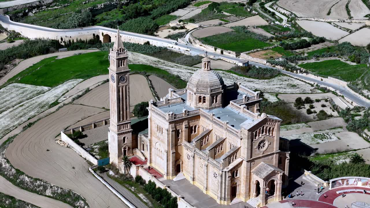 Ta' Pinu Basilica Aerial View stands amidst the lush green fields of Gozo Malta during a bright spring morning featuring golden limestone architecture and a tall bell tow