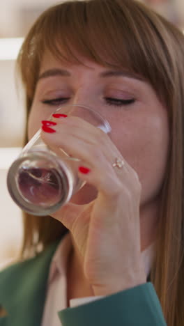 mujer bebe agua de un vaso mirando hacia un lado y sonriendo en un fondo borroso. el cliente se siente mejor después de tomar la píldora en la tienda de primer plano en cámara lenta