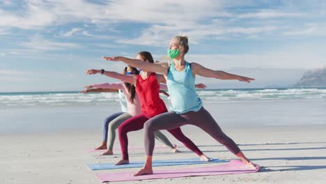 grupo de diversas amigas con máscaras faciales practicando yoga en la playa