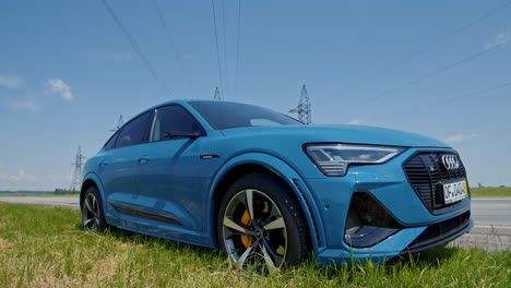 new model of audi e-tron car outdoors. luxury electric car on the background of high voltage towers. blue sportive model of e-tron auto for clean environment.