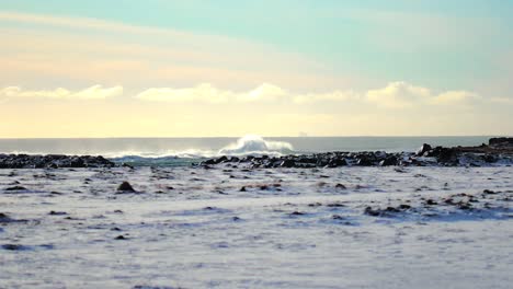 slow motion shot of large wave breaking in distance in iceland in the winter during a bright day