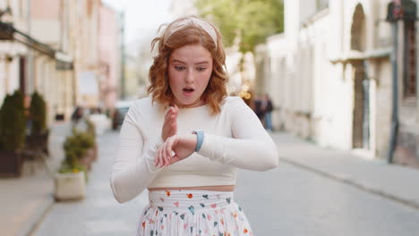 redhead woman worrying to be punctual with anxiety checking time on watch running late to work