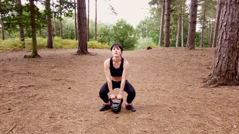 girl working out with a kettle bell in the woods