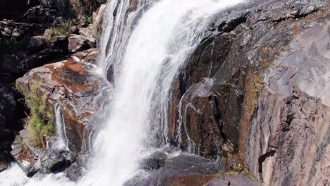 aerial drone shot panning through waterfall and showing a giant volume waterfall with dry rocks in the foreground