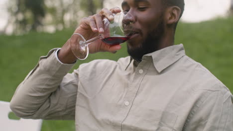 man taking a glass of wine from a table and drinking it during a garden party in the park