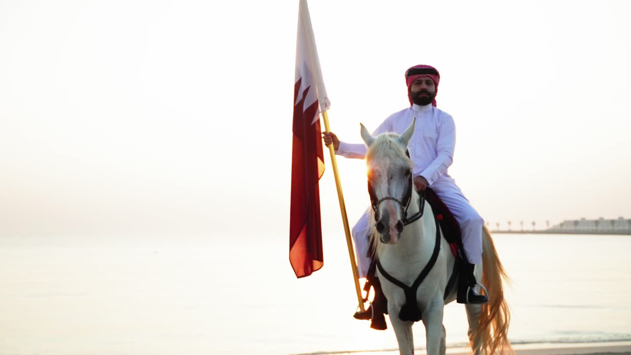 Un cavaliere a cavallo che tiene la bandiera del Qatar vicino al mare-3