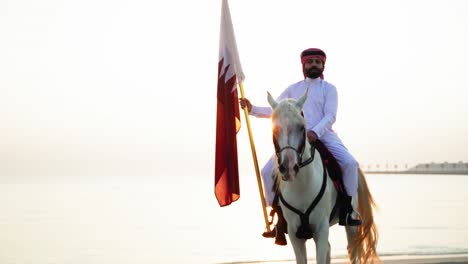 Un-Caballero-A-Caballo-Sosteniendo-La-Bandera-De-Qatar-Cerca-Del-Mar-3