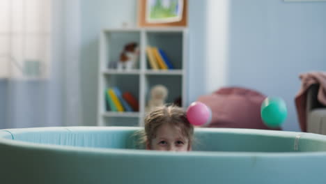 preschooler girl hides in dry pool tossing up colored balls