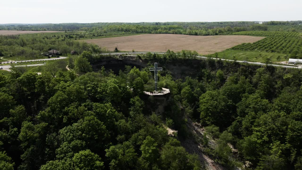 Aerial orbit shot of cross standing on hill surrounded by green forest trees at Devil's Punch Bowl, Ontario