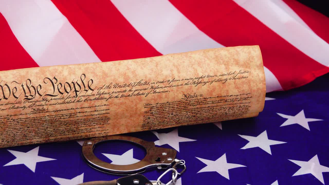 Symbolic image of handcuffs restraining the US Constitution against the backdrop of the USA flag representing the tension between freedom rights justice and the rule of American law