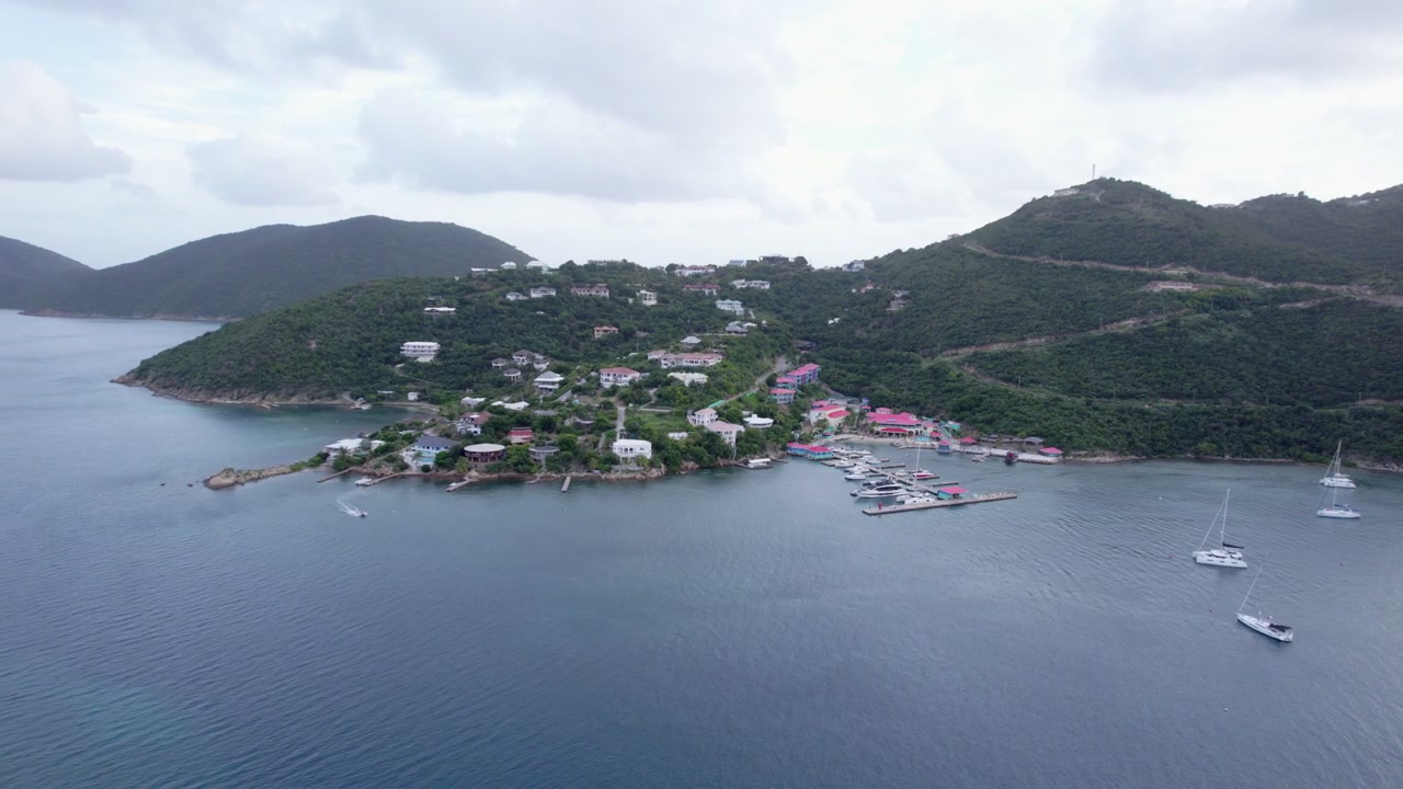 Una veduta aerea di una giornata nuvolosa su Leverick Bay nelle Isole Vergini Britanniche, che cattura una barca che entra con grazia nella baia con uno scenario costiero mozzafiato e acque tranquille.