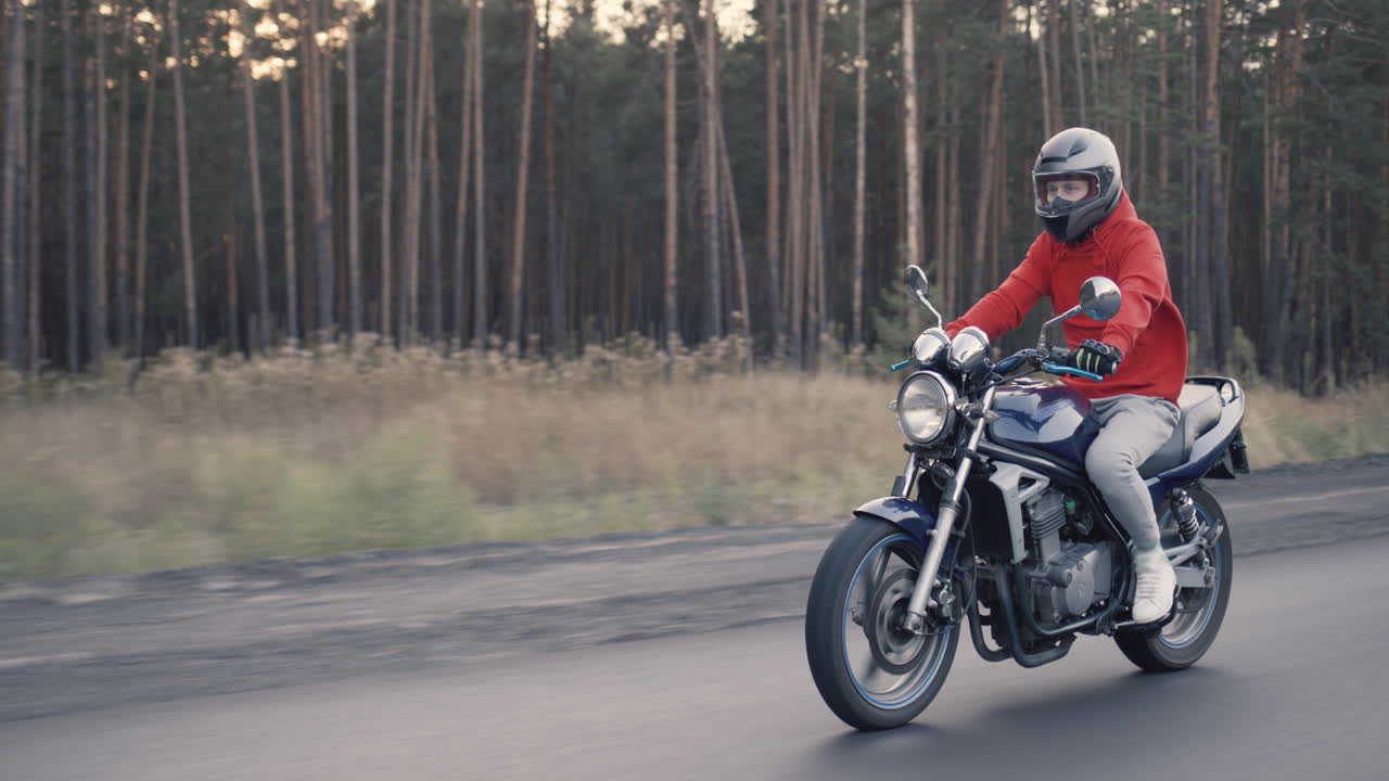 joven motociclista recorre rápidamente la carretera a lo largo del bosque 1