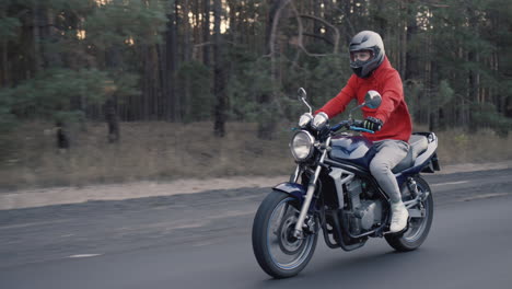 young motorcyclist quickly rides along the road along the forest 1