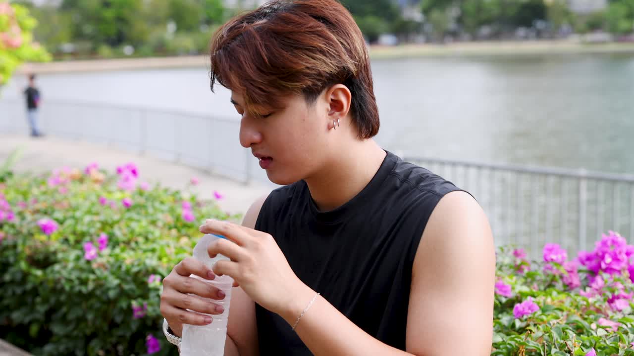 晴れた日の公園で、健康的なタイ人男性が屋外でウォーターボトルから水を飲んでいます。