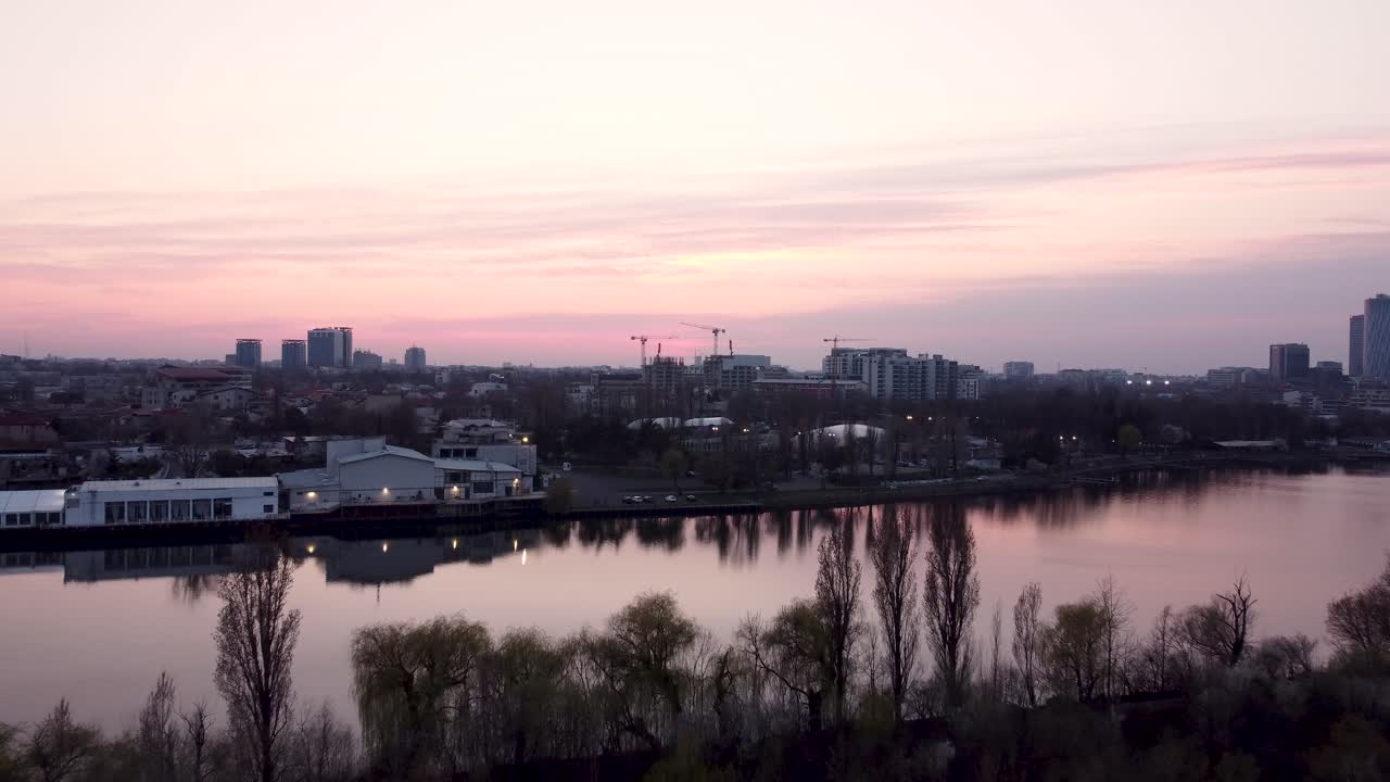 Ilmakuva vaaleanpunaisesta auringonlaskusta kaupungin keskustan ja järven yllä