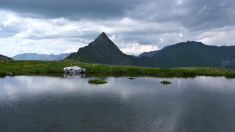 lago alpino remoto con hierba verde y montaña puntiaguda en el fondo