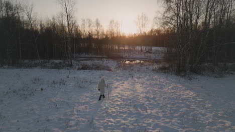 Un-Hombre-Con-Chaqueta-Blanca-Camina-Hacia-El-Atardecer-En-Un-Campo-Nevado