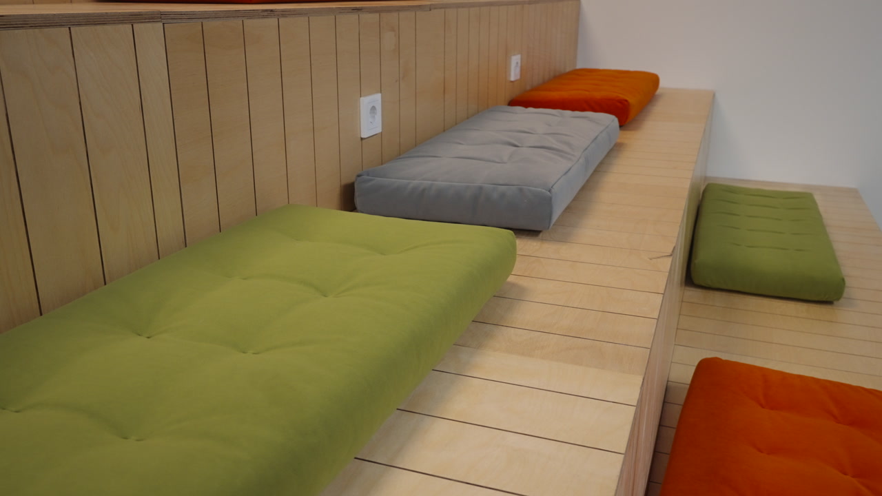 Green And Orange Cushions On Bench With Gray Pad On Wooden Platform, Vertical Wood Panel Wall With Builtin. Creative