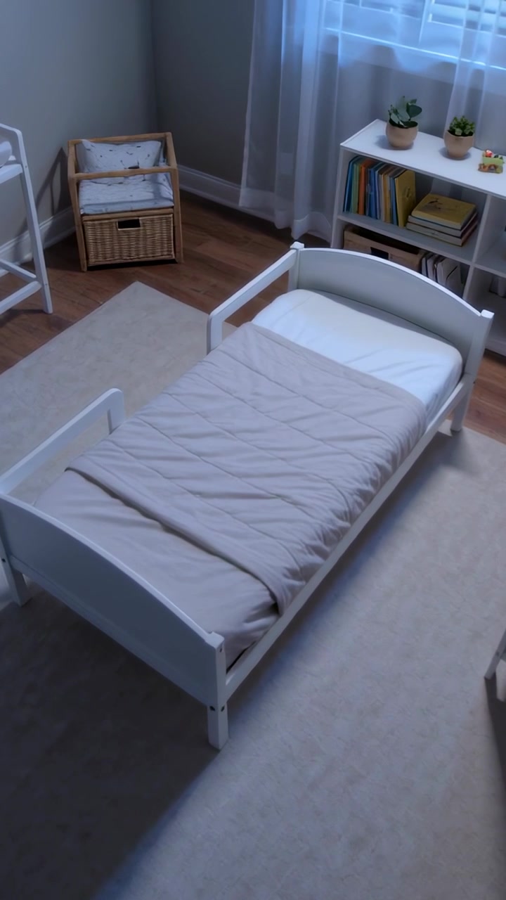 Video verticale: Telecamera che si inclina, portando avanti un piccolo lettino bianco per bambini nella cameretta, con una trapunta beige.