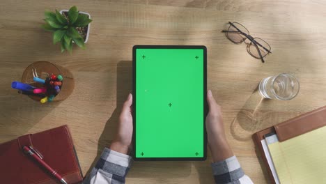 persona sosteniendo una tableta con una pantalla verde en un escritorio de madera