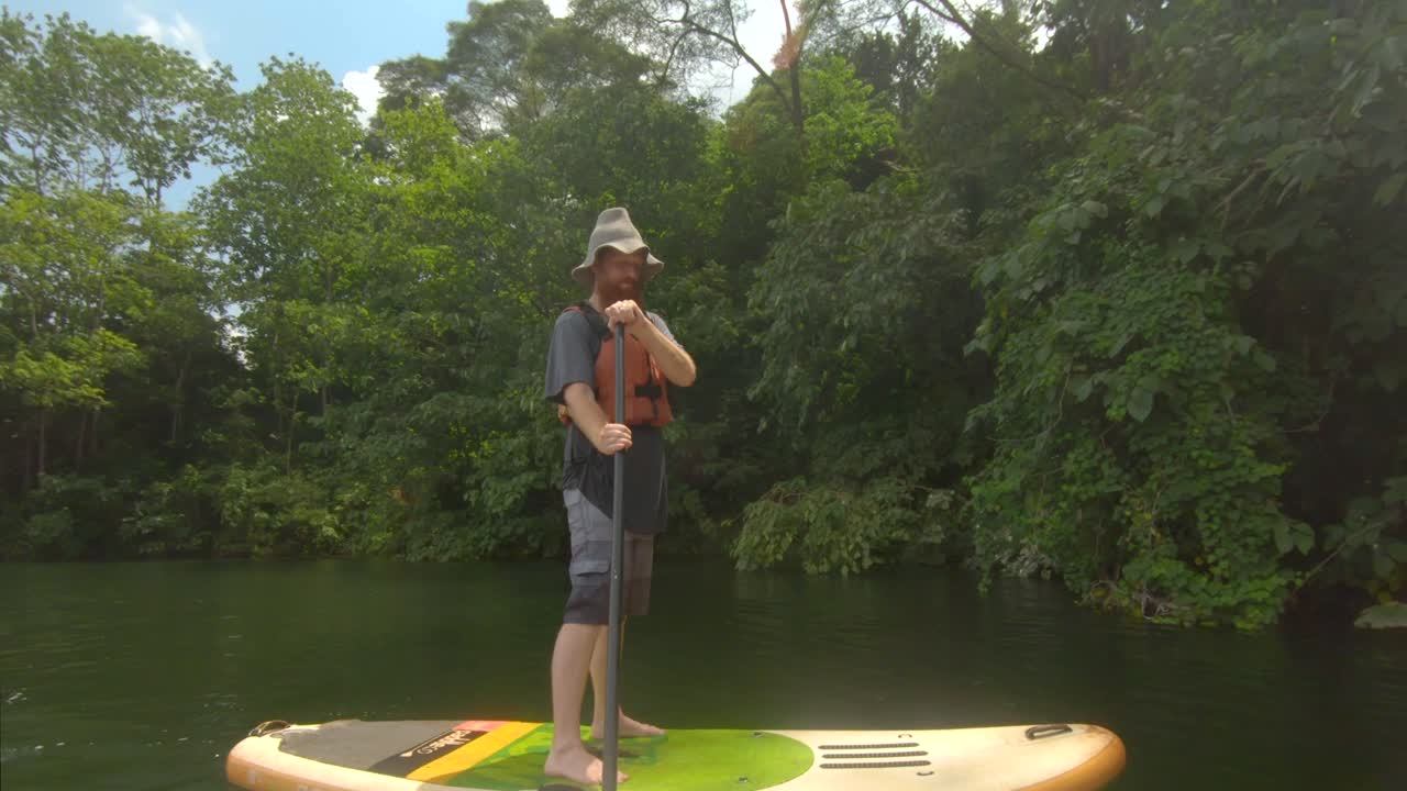 Un uomo barbuto dai capelli rossi sulle rive del fiume Nilo nell'Africa tropicale su una tavola da stand up paddle