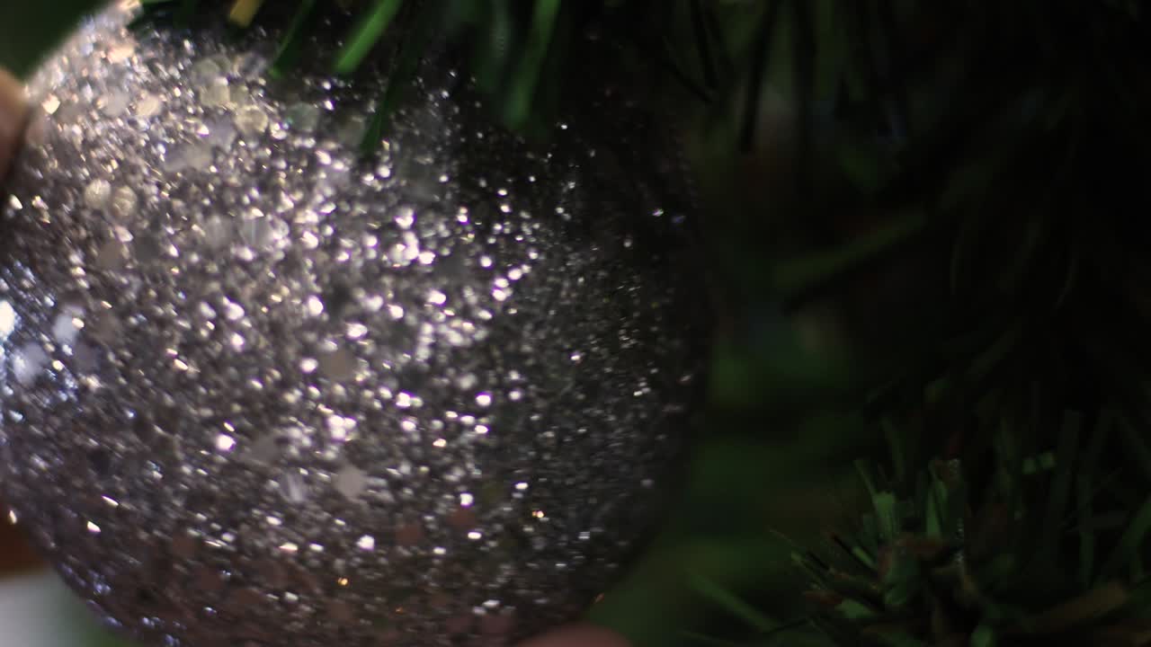 4k Close up, asian male hand holding  silver glitter ball on Christmas tree, new year decorating, holidays events, DIY, happiness, handheld shot, hobbies, checking twisting, sphere, green fir tree,