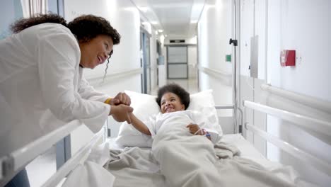 african american female doctor holding hand of girl lying in hospital bed in corridor, slow motion
