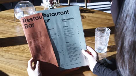 Blick-über-Die-Schulter-Einer-Frau,-Die-Am-Restauranttisch-Die-Speisekarte-Liest