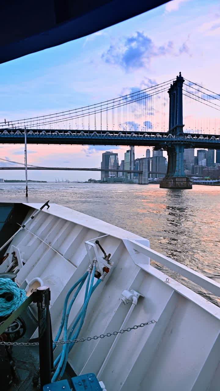 On board of the boat travelling by the East River. Low angle view at the Manhattan Bridge and New York skyline at sunset time. Vertical video