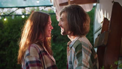 happy brunette girl together with her brunette boyfriend in plaid shirts stand next to each other close and look at each other near their trailer during a picnic in a camp outside the city in the summer