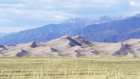 stunning late summer early fall view of the great sand dunes national park colorado rockies mountain sandy 14er peaks crisp golden yellow tall grass wind clouds blue sky mid day cinematic pull