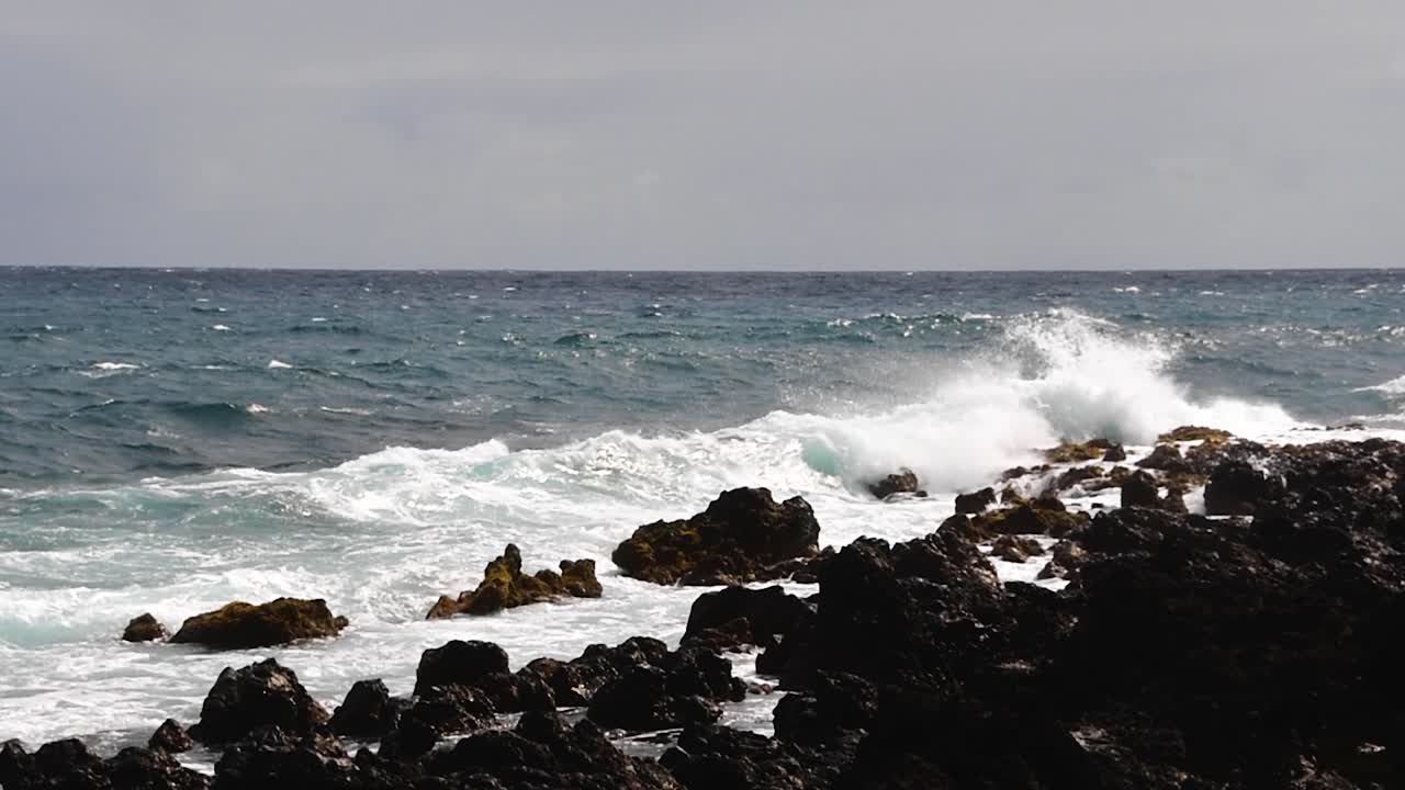 Una leggera panoramica verso il basso sulle onde che si infrangono sulla roccia vulcanica hawaiana, Maui, Hawaii.