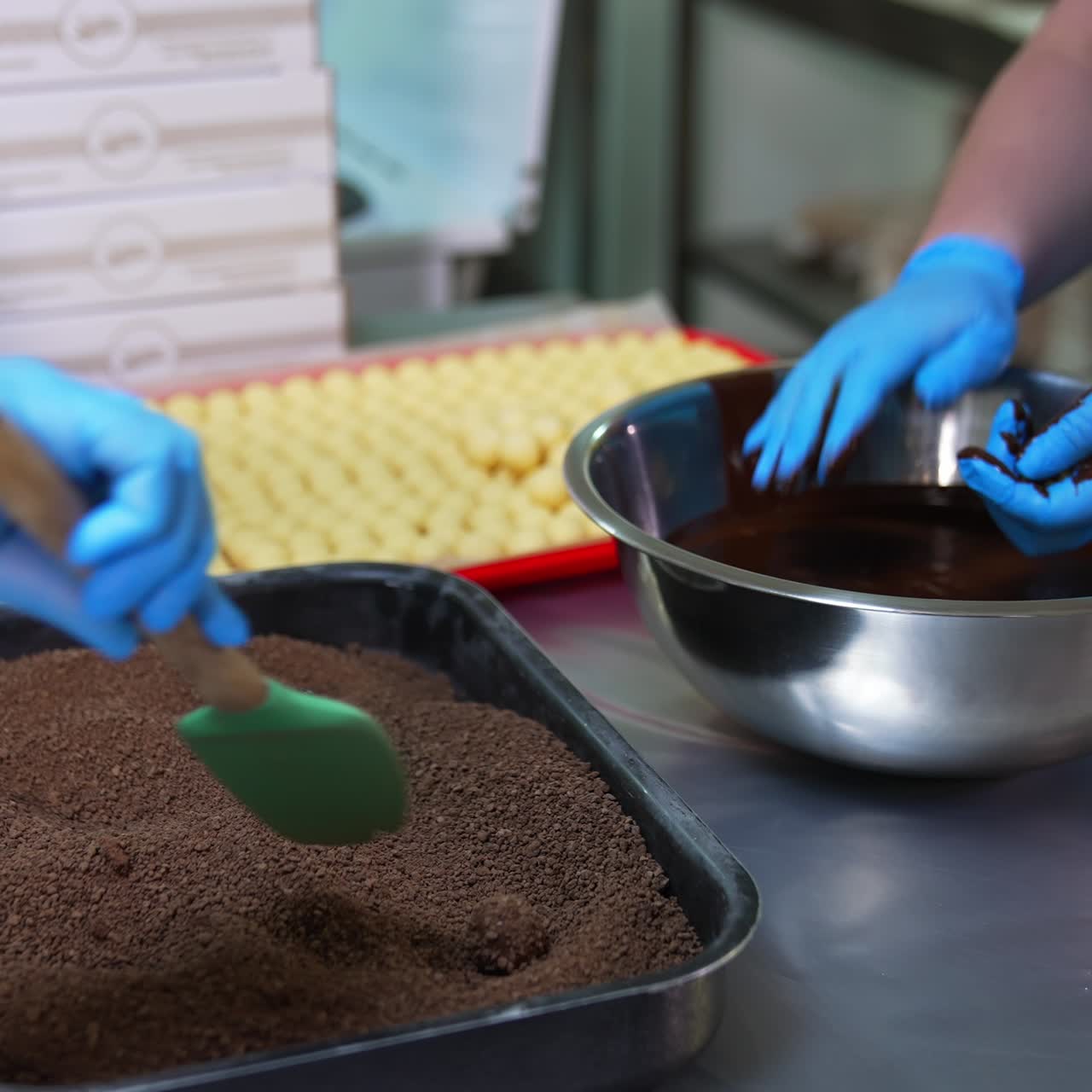 Female worker in latex gloves covers creamy candies with chocolate. Other worker coats chocolate balls with cocoa sprinkling. Candy making concept