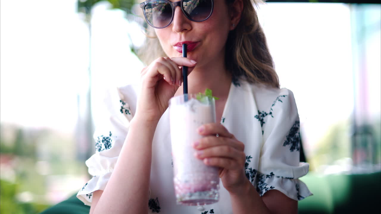 Woman mixing and drinking a strawberry drink with a black straw at a restaurant
